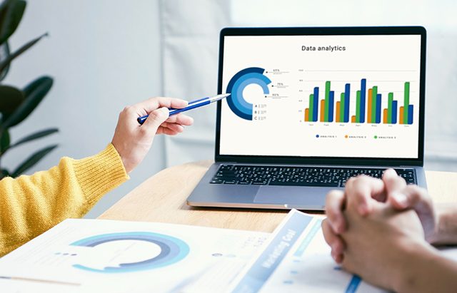 Person pointing at a laptop displaying a data analytics dashboard with charts and graphs.